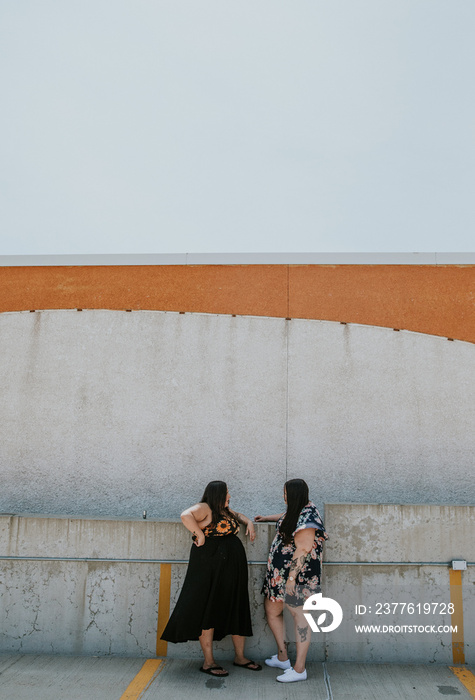 2 women stand against a concrete wall talking