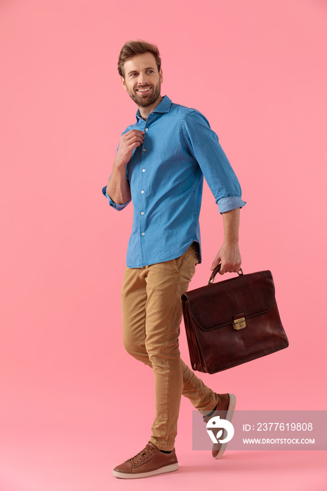 happy casual man holding suitcase and fixing shirt