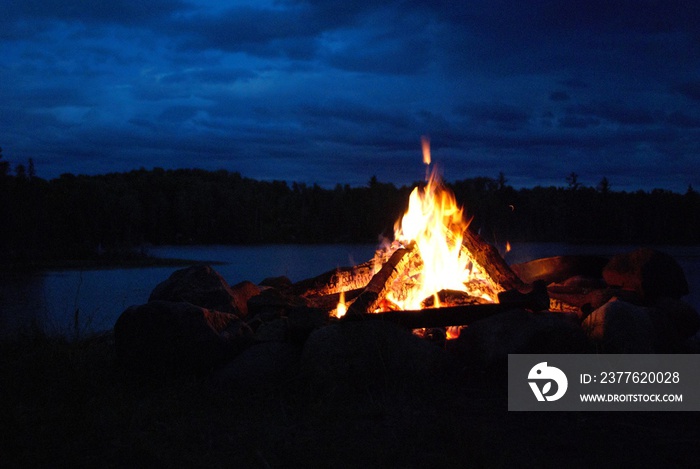 camp fire burning in a fire pit next to the lake