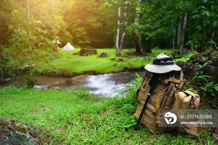 backpack with SOS bag and hiking walking pole with hat for trekking and camping tent on stream with tree in green grass jungle for holiday relax and vacation travel trip with adventure nature morning