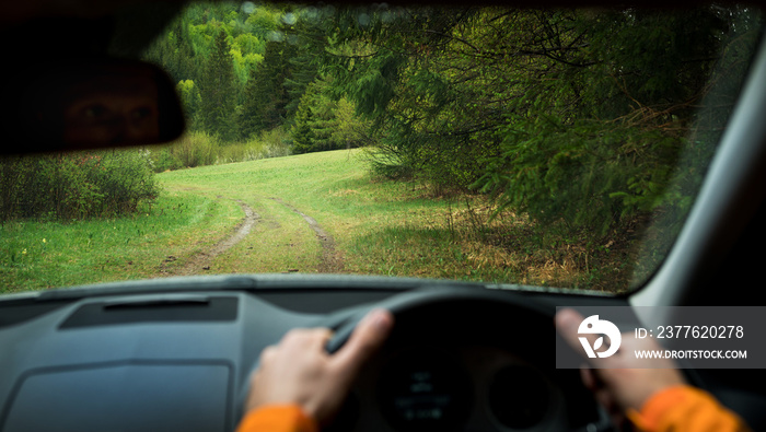 Driver driving a modern off road right hand drive RHD car on the mountain green forest country road. Face reflecting in inside mirror. POV inside car windshield view point. Safely auto driving concept