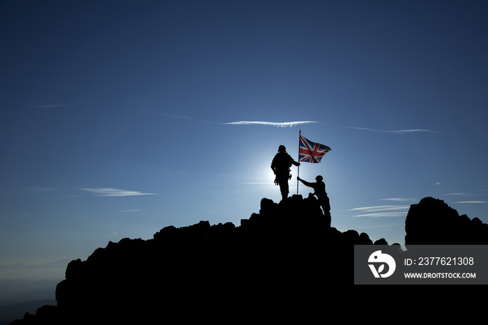 Two soldiers raise the flag of Great Britain on top of the mountain