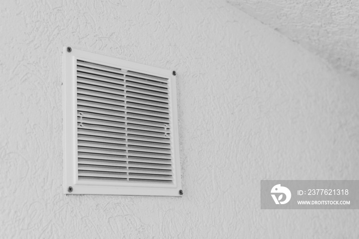 Grilled window covering an air conditioning system evacuation hole on a white textured wall