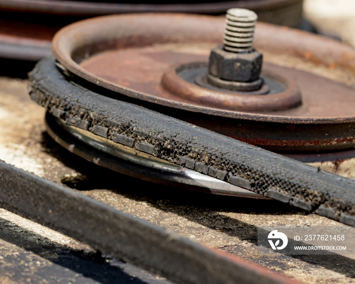 An old, cracked drive belt and pulley on a lawn mower deck needing maintenance