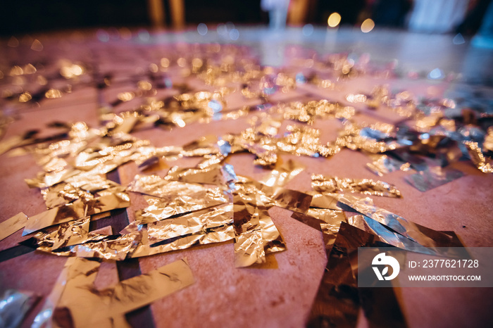 Golden Confetti on a wooden floor reflecting red stage spotlight causing colorful glow