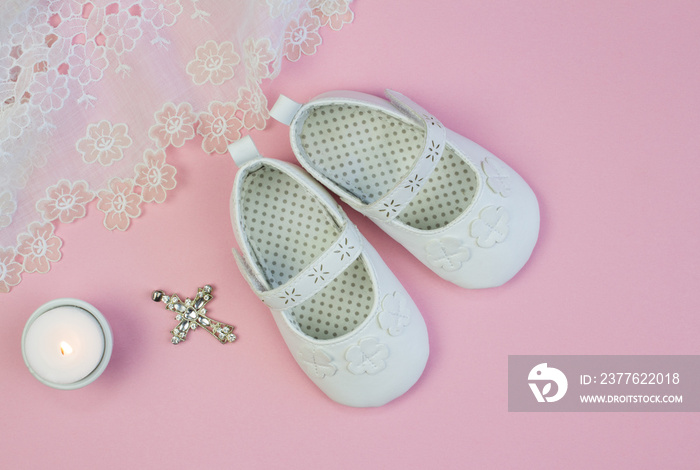 Pair of white baby booties on pink background with vintage lace christening dress