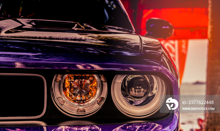 Closeup headlight lamp of purple classic vintage car on blurred red background.