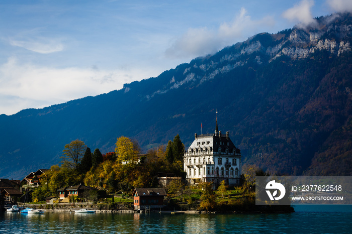 View across Brienzersee Lake, Switzerland with the white facade of Iseltwald castle reflected in the calm waters of the lake and Niesen mountain rising up in the far distance