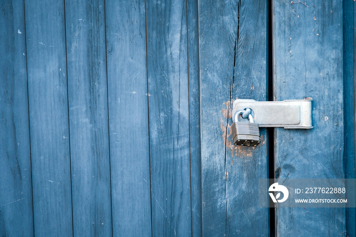 Old padlock and blue boards keep door locked.