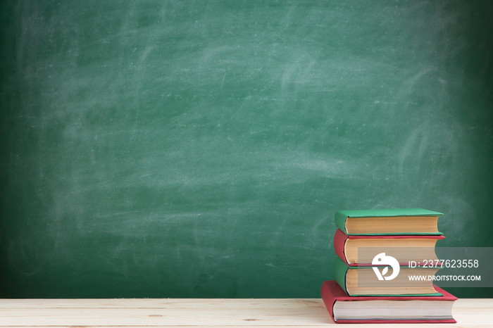 Education and reading concept - group of colorful books on the wooden table in the classroom, blackboard background