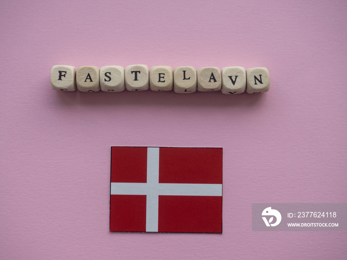 Norwegian carnival concept background. Pink background with text Fastelavn on wooden cubes and with flag of Denmark. Copy space.