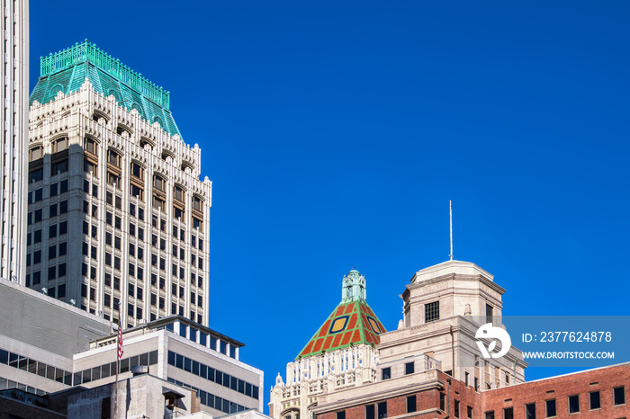 View of rooftops of downtown Tulsa Oklahoma -mixture of Art Deco and modern buildings with an American flag against very clear blue sky