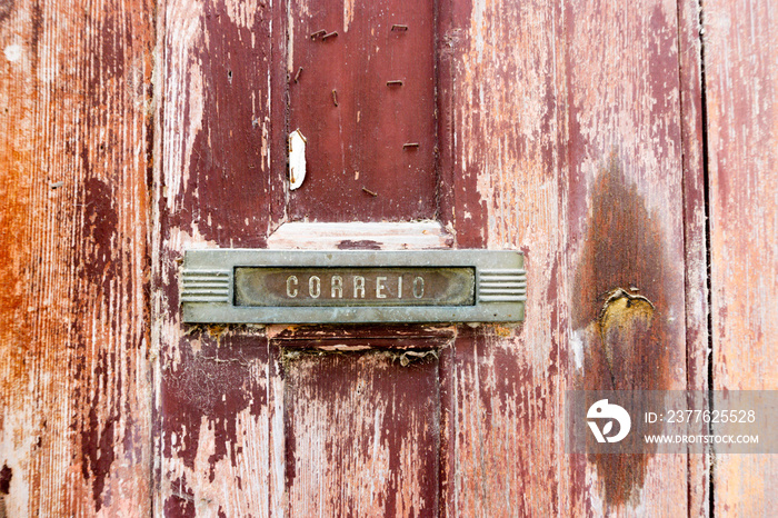 Detail of the mail slot of a vintage red worn wood door.