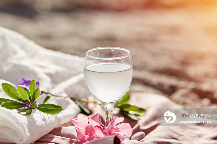 Gin tonic cocktail in wine glass on beach with flowers and sunlight. Delicate silk materials and bokeh background. Refreshing summer concept. High quality photo