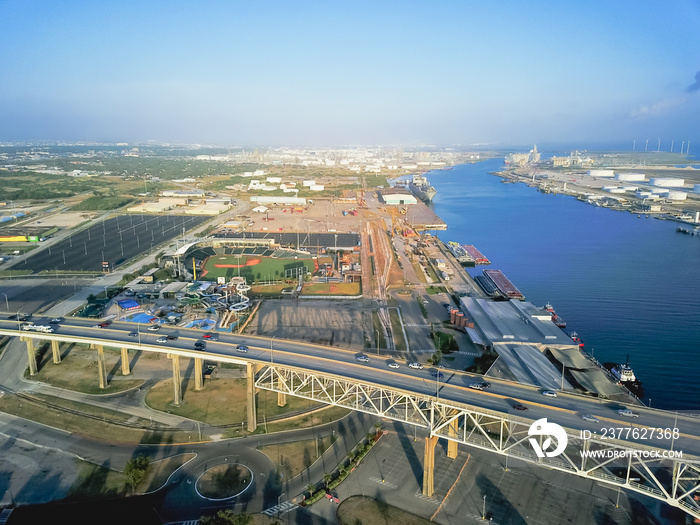 Aerial view of Corpus Christi Harbor Bridge with row of oil tanks and wind turbines farm in distance. A through arch bridge crosses the Corpus Christi Ship Channel