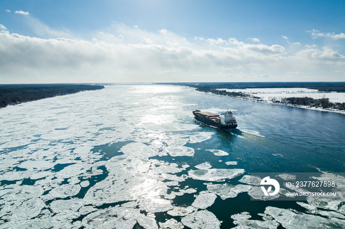 Aerial view of a container ship going upstream through winter ice in the St. Lawrence River near the port of Montreal in Canada