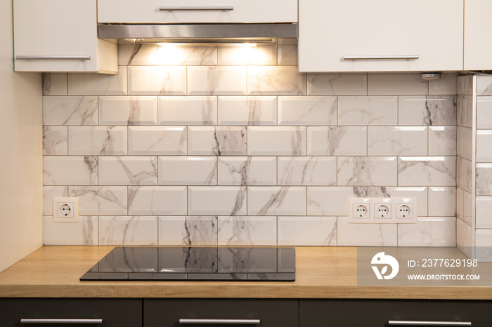 Modern kitchen view with empty induction cooker hob in wooden counter and white tile backsplash and cabinets