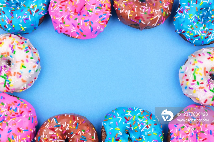 Frame of assorted donuts with frosting and sprinkles against a pastel blue background