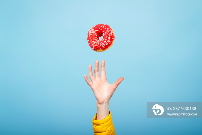 Hand catch a donut with red icing. Blue cardboard background. The concept of baking, handmade. Flat lay, top view