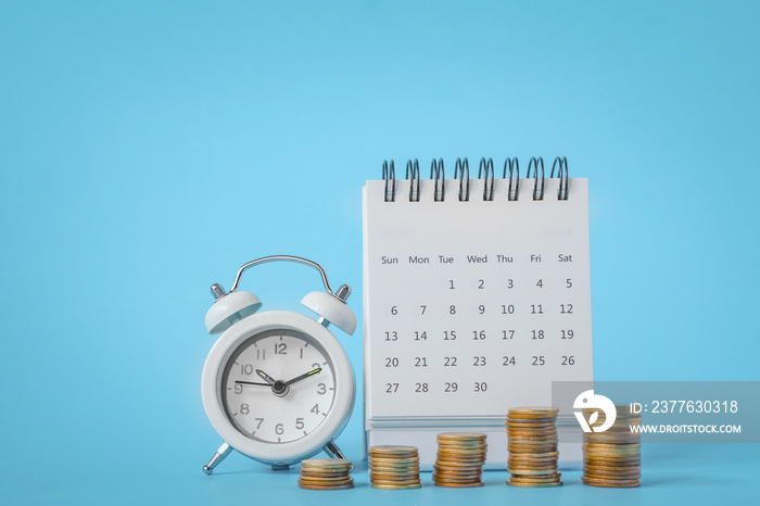 stack of coins , white analog clock and white calendar on grunge blue paper background for business and finance background