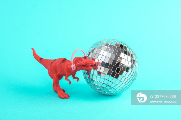 Toy red dinosaur tyrannosaurus rex with disco ball on a turquoise background. Minimalism creative layout