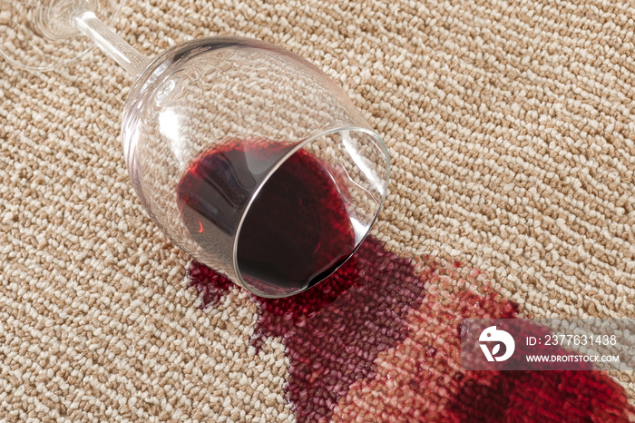 Home mishap and domestic accident concept with close up of  a spilled glass of red wine on brown carpet