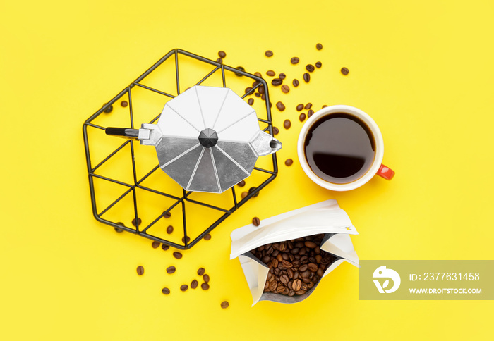 Geyser coffee maker on grid, cup of coffee and bag with beans against yellow background