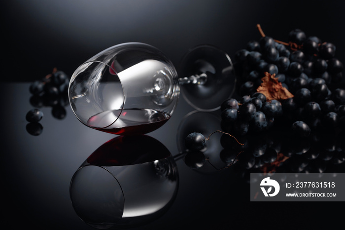 Blue grapes and wine glass with red wine on a black reflective background.