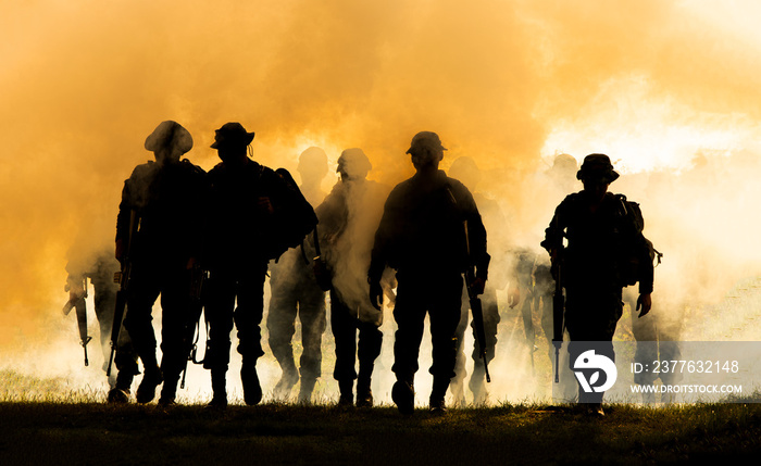 Silhouettes of army soldiers in the fog against a sunset, marines team in action, surrounded fire and smoke, shooting with assault rifle and machine gun, attacking enemy