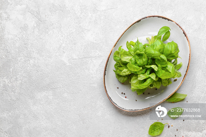 Plate with fresh basil leaves on light background