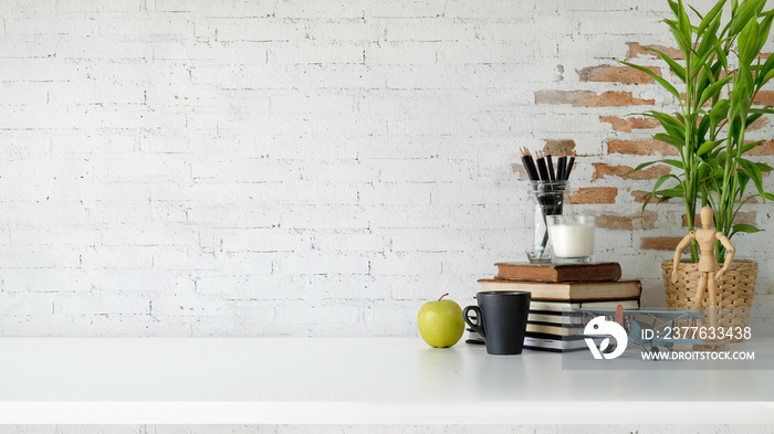 Loft workspace with books, coffee mug and copy space over white brick wall.