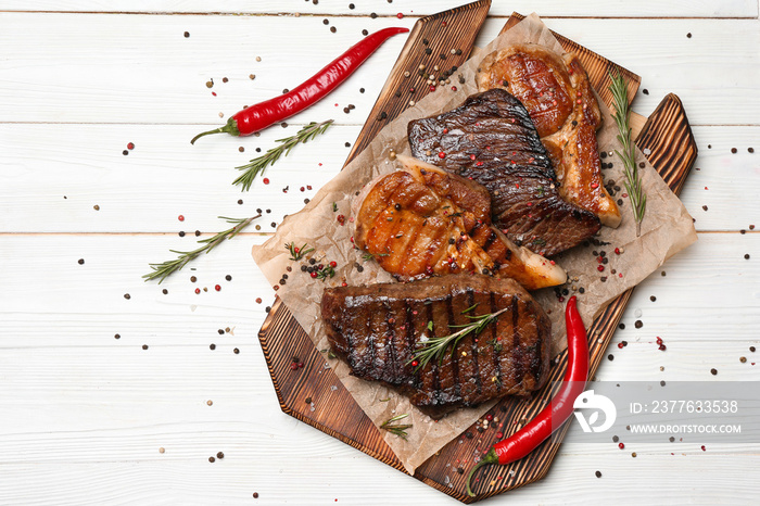 Wooden board with different tasty cooked meat and spices on white table