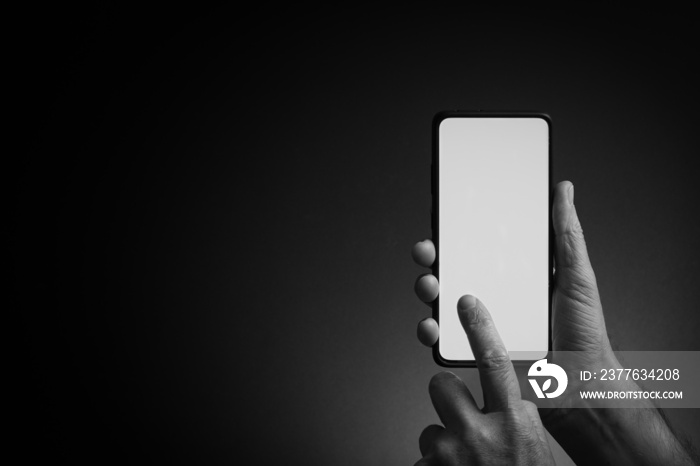 Man’s hand holding smartphone with blank screen isolated on dark background