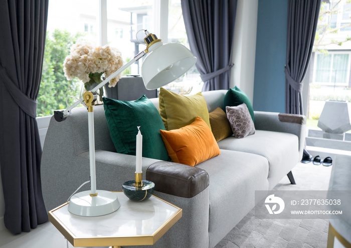 White living room interior with yellow , blue and pink pillows on sofa. golden table lamp aside.