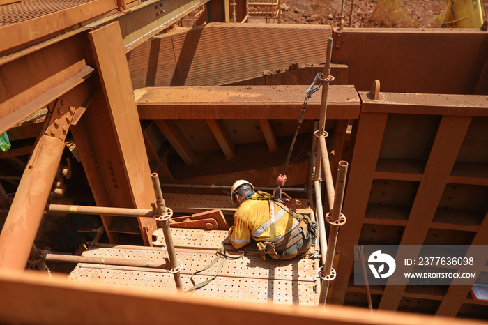 Scaffolder seating wearing safety helmet, fall arrest harness using clipping retractable device on the back of their safety harness loop attached to scaffold pole to preventing falling off working