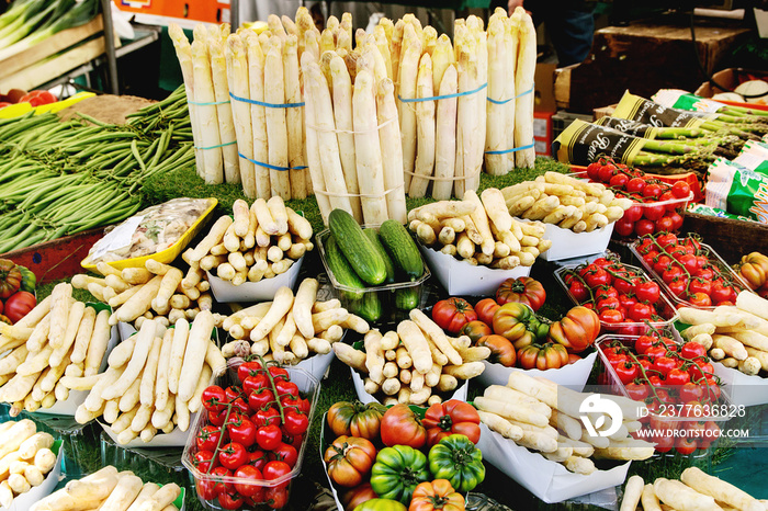 Market stall with fresh spring season vegetables at Parisian street farmers market. White asparagus, tomatoes, cucumbers.