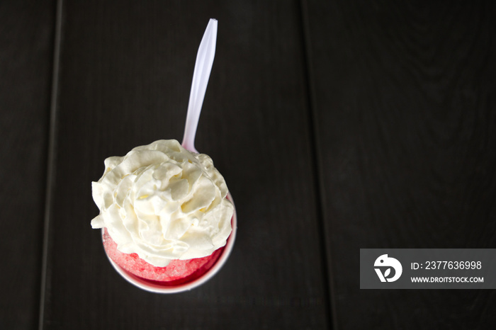 A vibrant red cherry snowball or snocone shaved ice summer treat or dessert with whipped cream on top