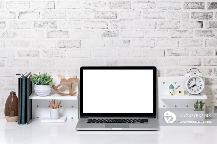 Creative workspace with blank screen laptop computer and supplies on white top table and brick wall.