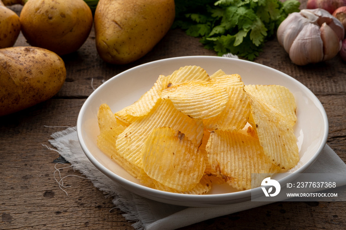 Fried wavy potato chips snack in white plate on wooden table