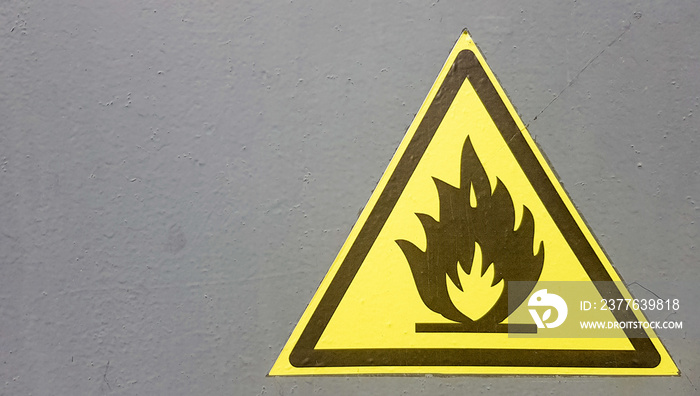 Fire warning icon, sign on a yellow label on a gray background. Flammable. Yellow triangle on a metal wall. Background with copy space.