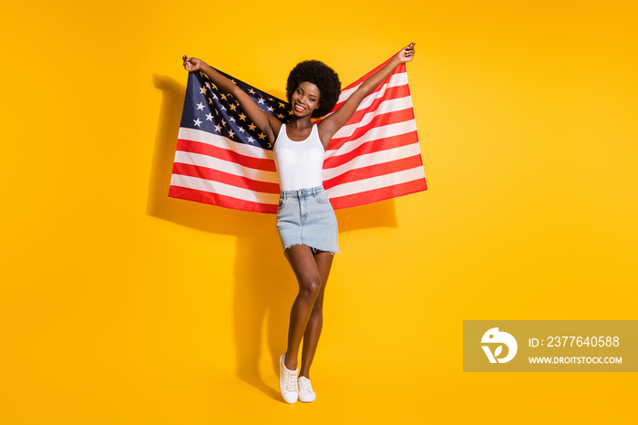 Full length body size view of pretty slim cheerful wavy-haired girl holding us flag having fun isolated over shine yellow color background