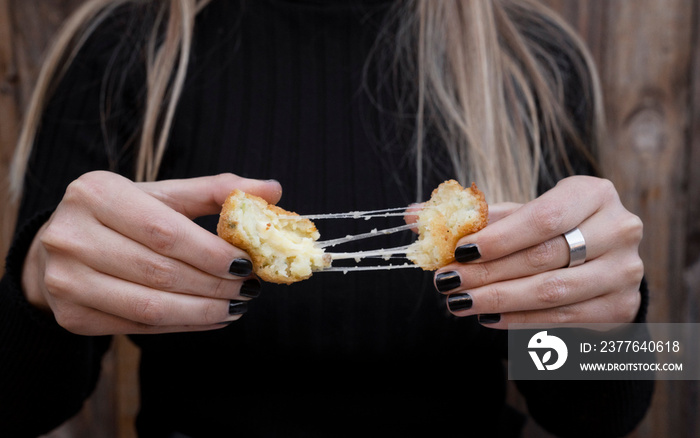 Food. Closeup view of a woman stretching the cheese of a sliced potato and mozzarella croquette.