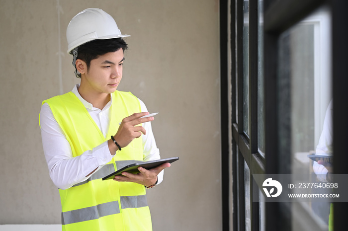 Young architect with helmet and tablet indoor at construction site, checklist concept.