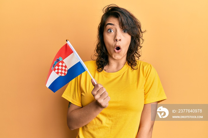 Young hispanic woman holding croatia flag scared and amazed with open mouth for surprise, disbelief face