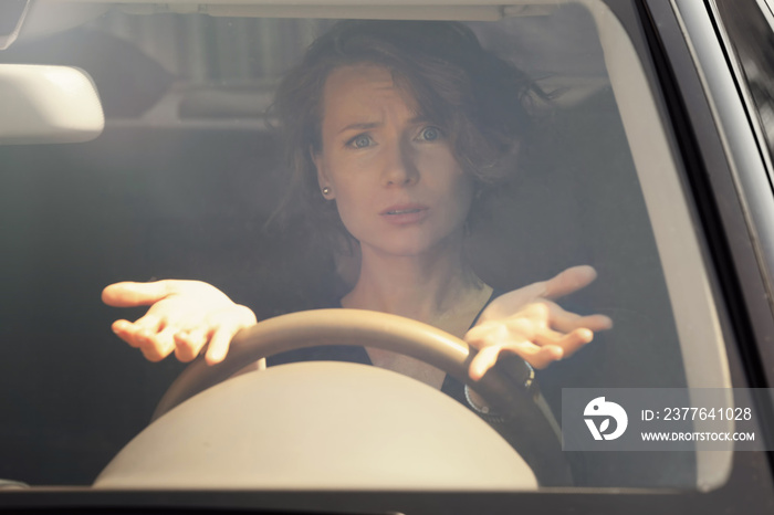 Emotional young woman driving a car, view from outside through windscreen