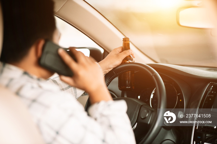 Drunk man holding bottle of beer and using smartphone while driving a car, campaigning for drunken not driving avoiding accidents on road, Don’t drink and drive concept.