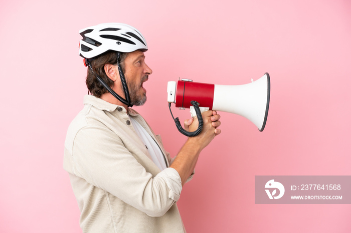 Senior dutch man with bike helmet isolated on pink background shouting through a megaphone