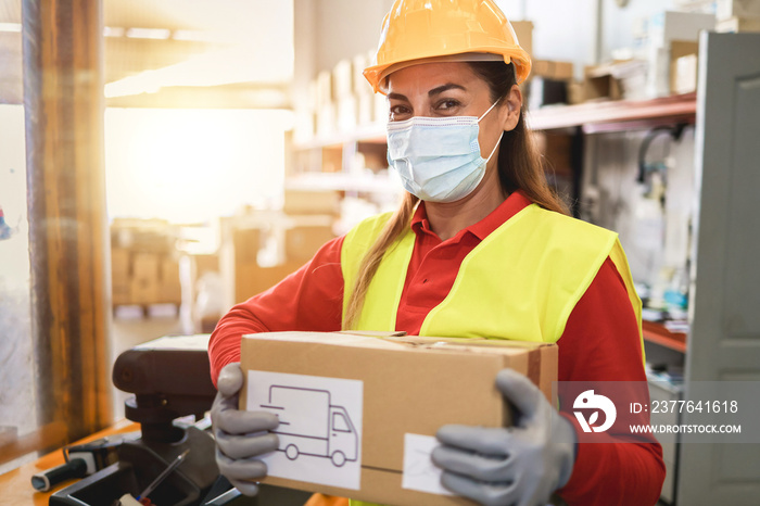 Hispanic warehouse worker woman holding delivery box while wearing safety mask - Focus on face