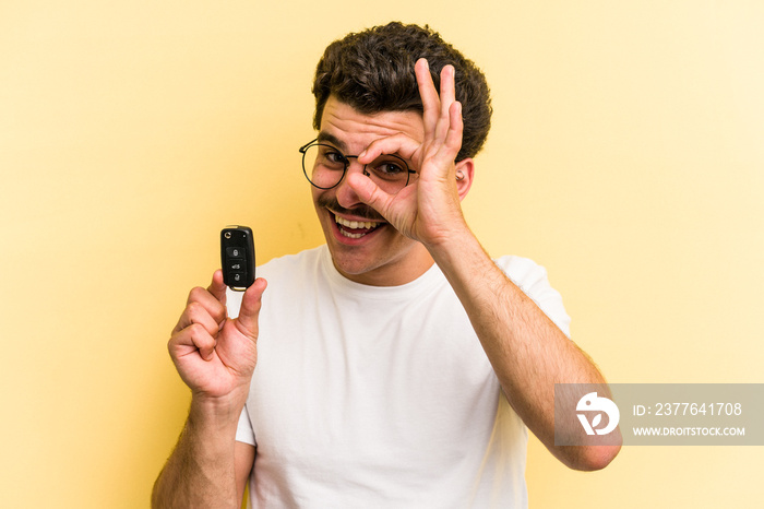 Young caucasian man holding car keys isolated on yellow background excited keeping ok gesture on eye.