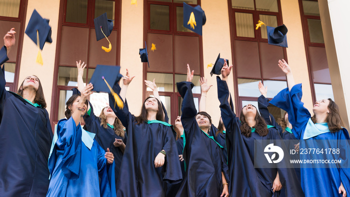 University graduates  throwing graduation hats in the air. Group of happy graduates in academic dresses near university building.